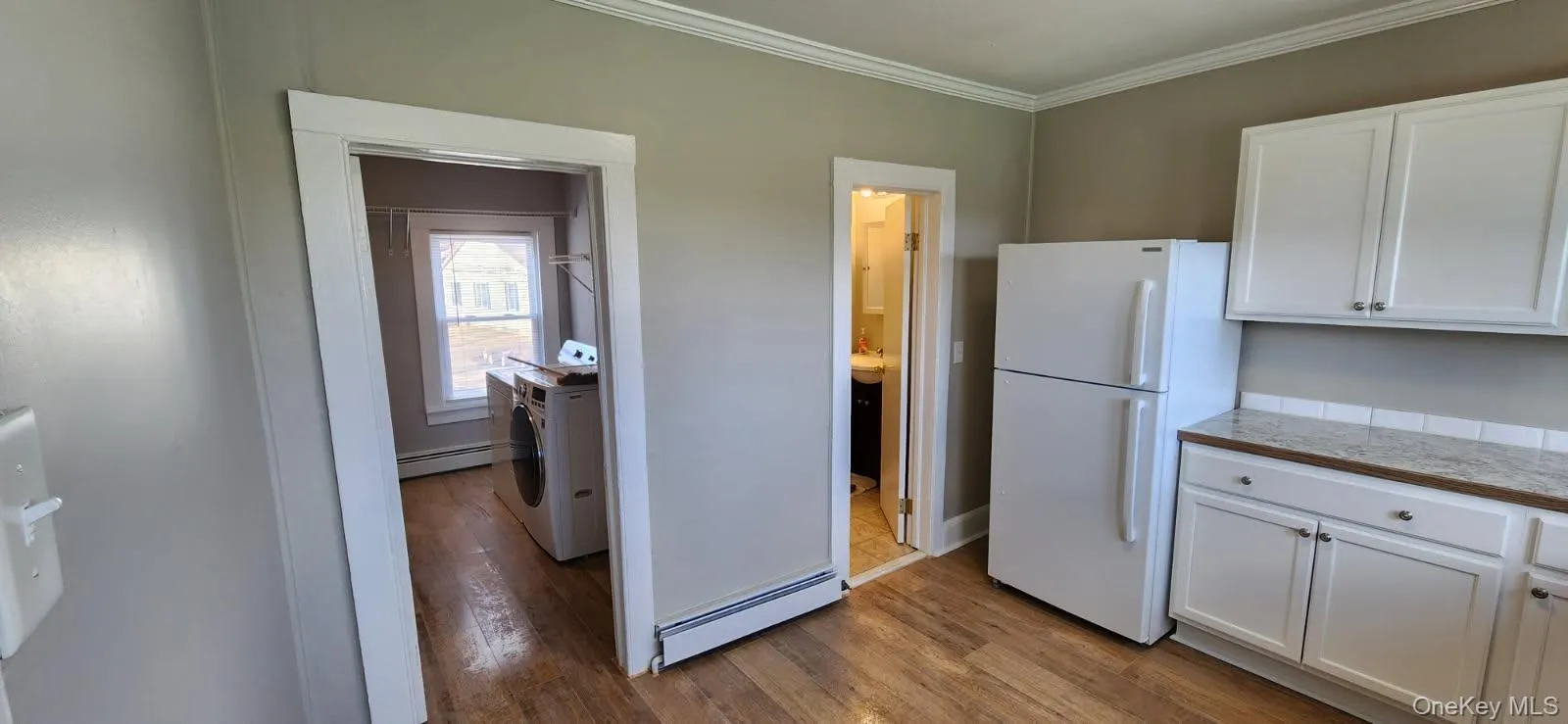 Kitchen featuring white cabinets, freestanding refrigerator, a baseboard heating unit, dark wood-type flooring, and ornamental molding Kitchen featuring white cabinets, freestanding refrigerator, a baseboard heating unit, dark wood-type flooring, and ornamental molding