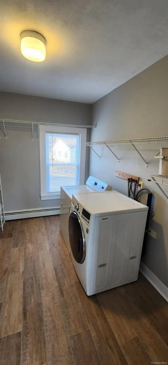 Laundry room featuring independent washer and dryer, dark wood finished floors, and a baseboard heating unit Laundry room featuring independent washer and dryer, dark wood finished floors, and a baseboard heating unit