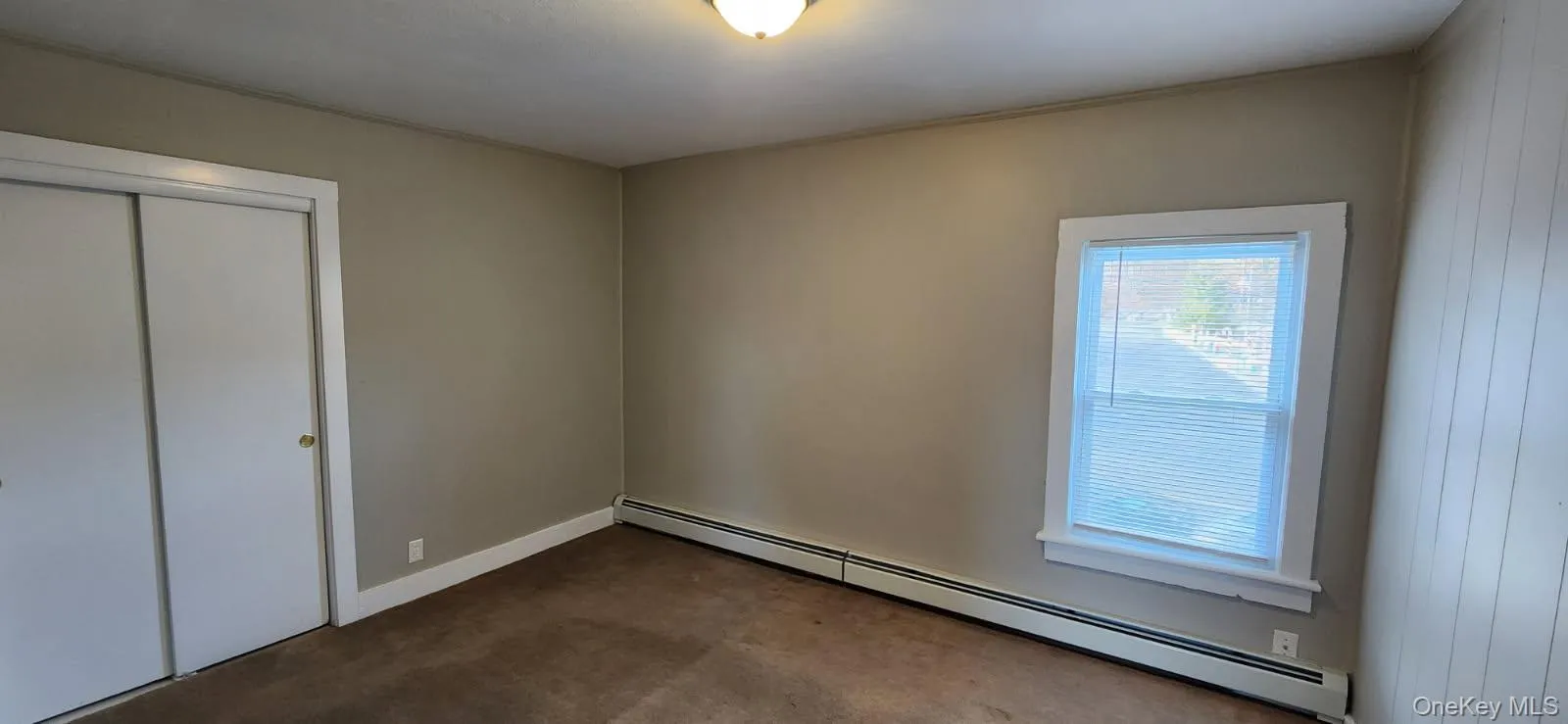 Unfurnished bedroom with baseboard heating, carpet flooring, and a closet Unfurnished bedroom with baseboard heating, carpet flooring, and a closet
