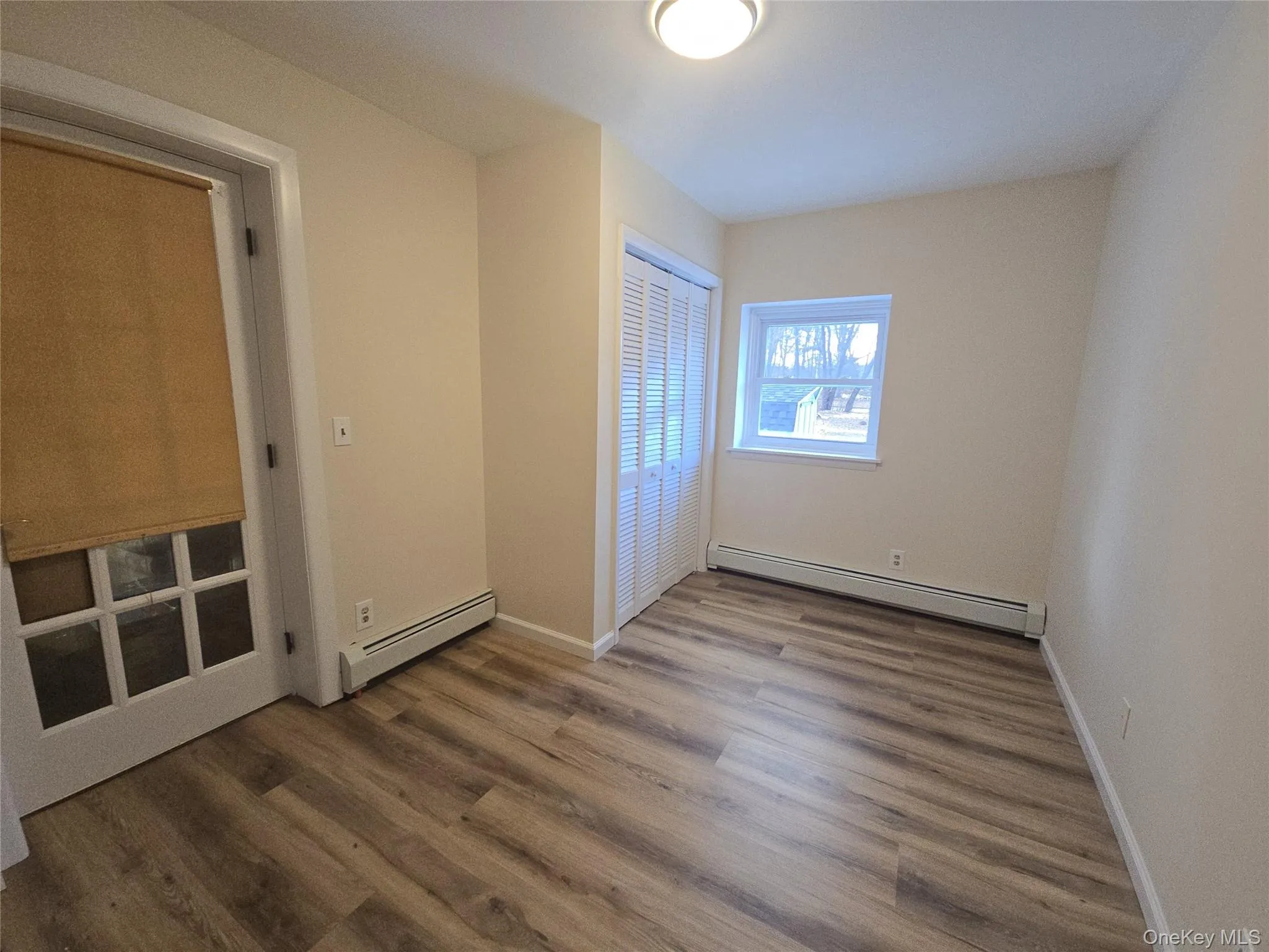 Unfurnished bedroom with a baseboard heating unit, dark wood-style flooring, and a closet Unfurnished bedroom with a baseboard heating unit, dark wood-style flooring, and a closet