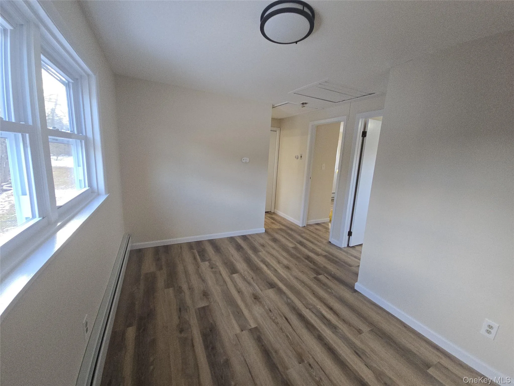 Empty room with baseboard heating, dark wood-style floors, and attic access Empty room with baseboard heating, dark wood-style floors, and attic access