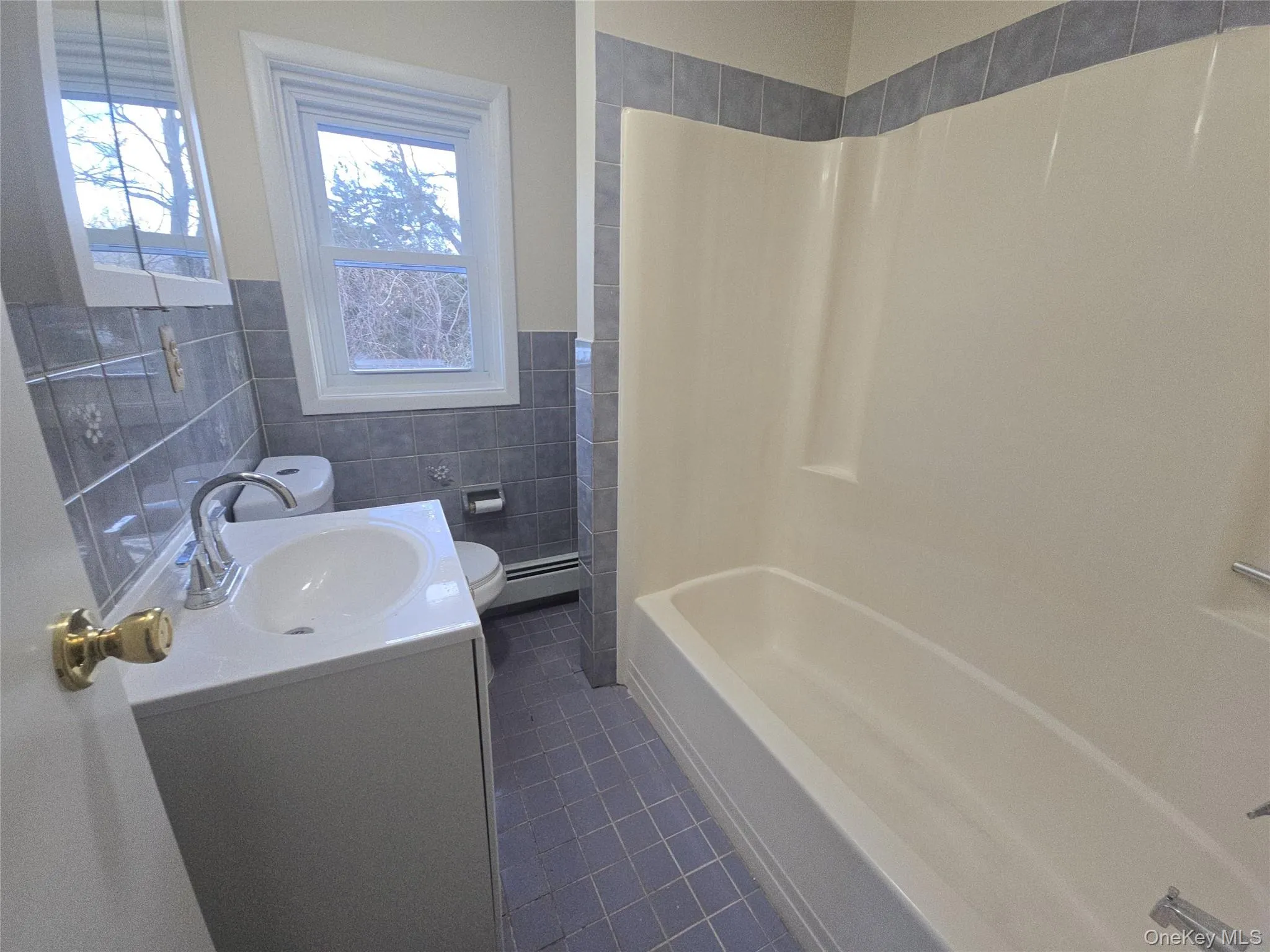 Full bath with vanity, tile walls, wainscoting, dark tile patterned flooring, and a baseboard heating unit Full bath with vanity, tile walls, wainscoting, dark tile patterned flooring, and a baseboard heating unit