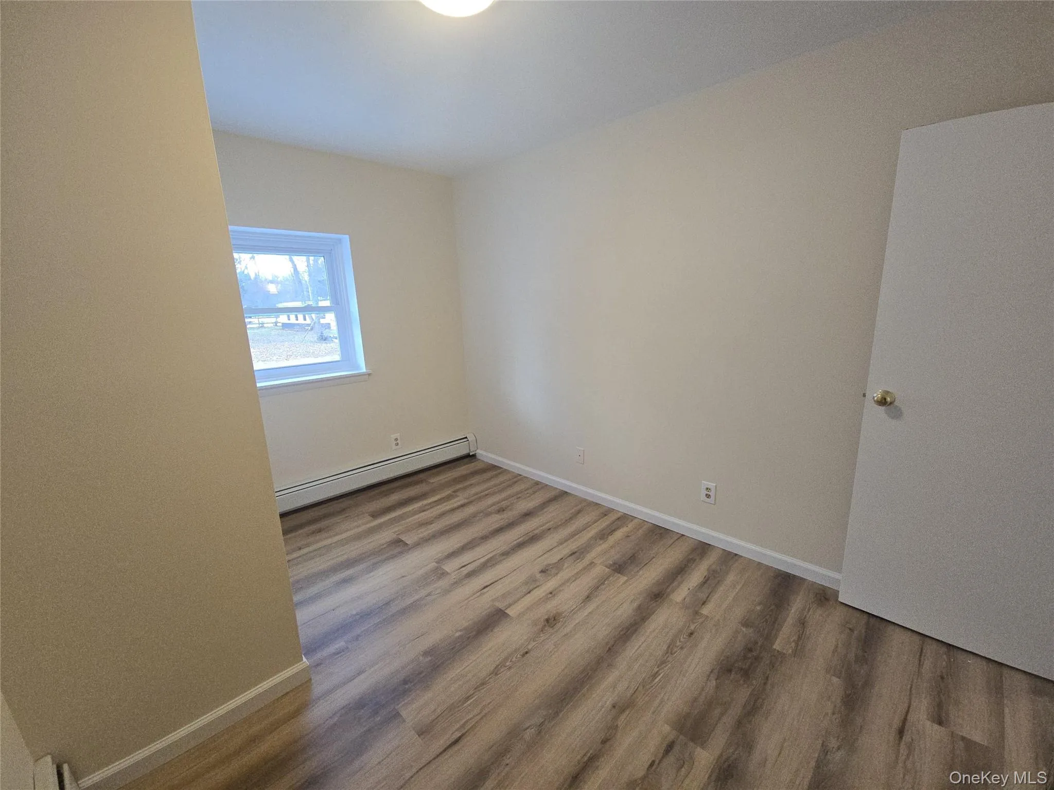 Unfurnished room featuring light wood-type flooring and baseboard heating Unfurnished room featuring light wood-type flooring and baseboard heating