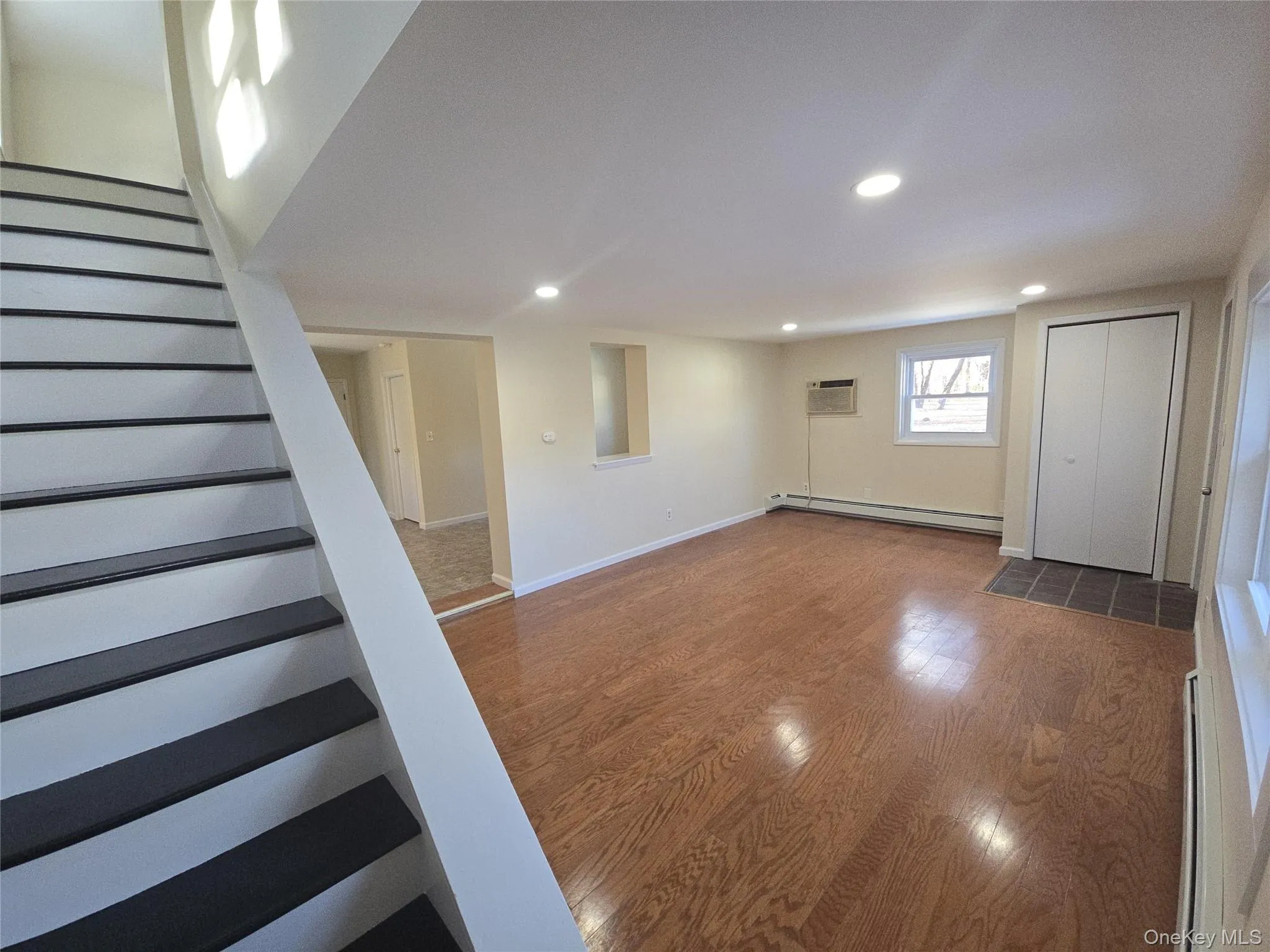 Below grade area featuring stairs, wood finished floors, recessed lighting, a baseboard radiator, and a wall mounted air conditioner Below grade area featuring stairs, wood finished floors, recessed lighting, a baseboard radiator, and a wall mounted air conditioner