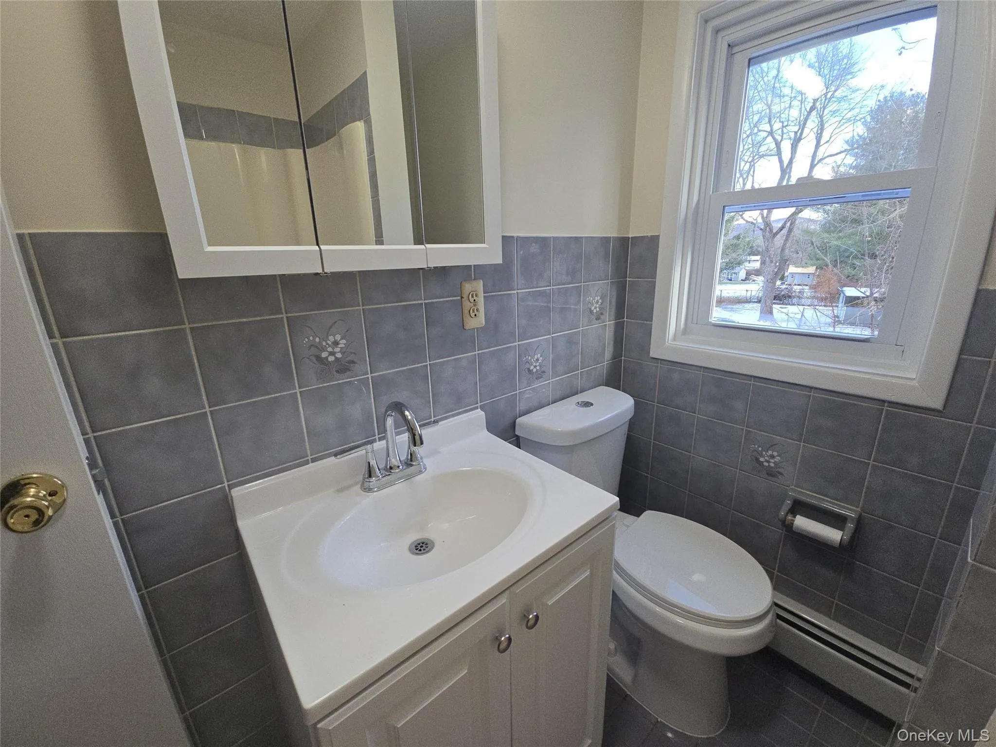 Full bath with vanity, a baseboard radiator, curtained shower, tile walls, and tile patterned flooring Full bath with vanity, a baseboard radiator, curtained shower, tile walls, and tile patterned flooring