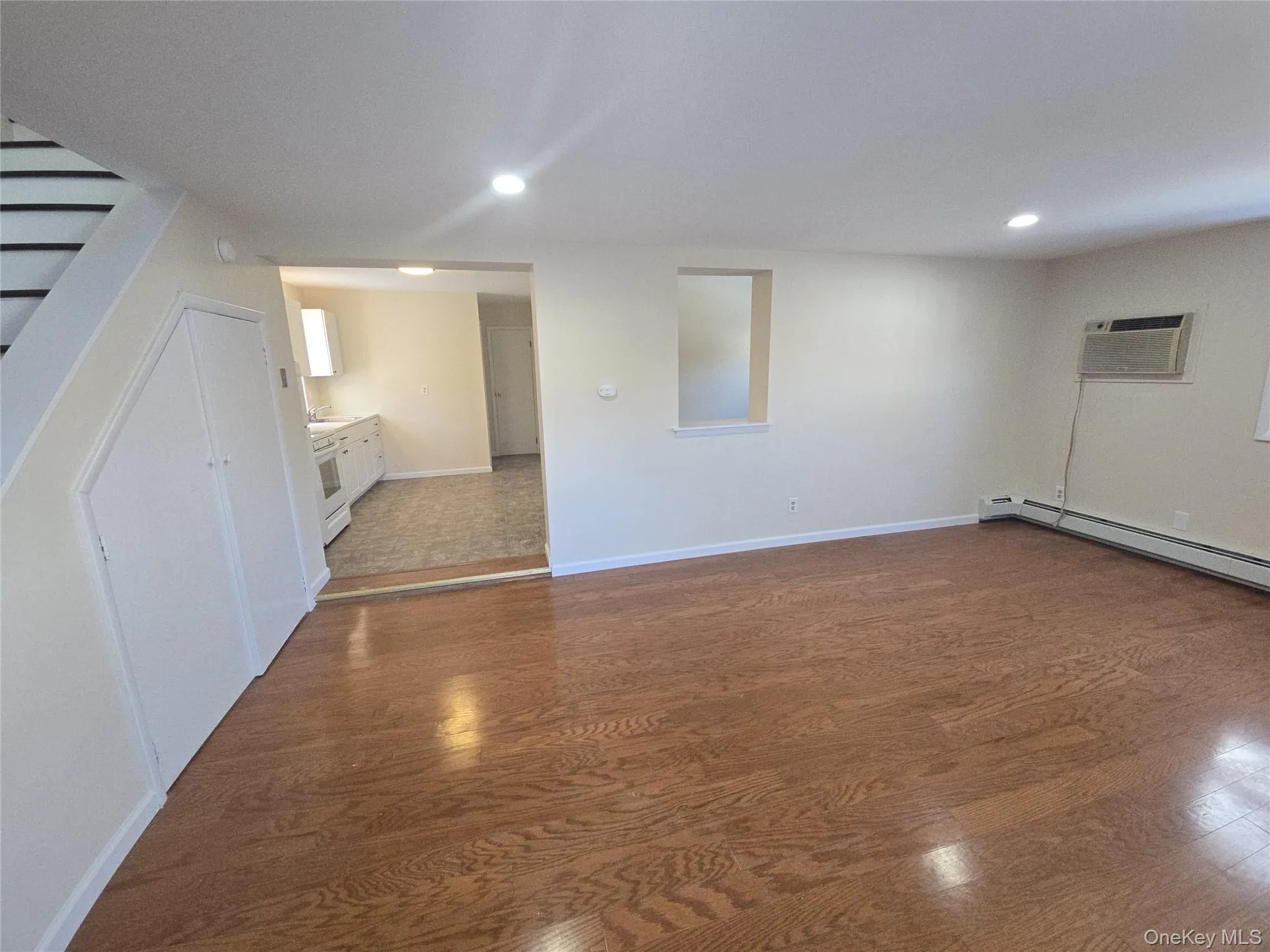 Basement with dark wood-style floors, recessed lighting, a wall mounted AC, and stairs Basement with dark wood-style floors, recessed lighting, a wall mounted AC, and stairs