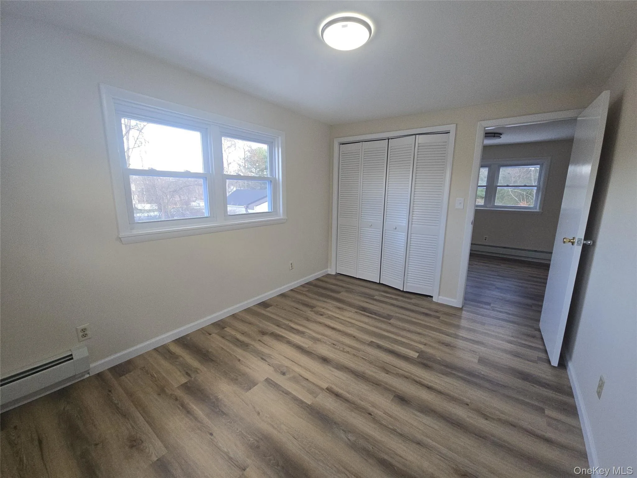 Unfurnished bedroom featuring a baseboard heating unit, wood finished floors, a closet, and baseboard heating Unfurnished bedroom featuring a baseboard heating unit, wood finished floors, a closet, and baseboard heating