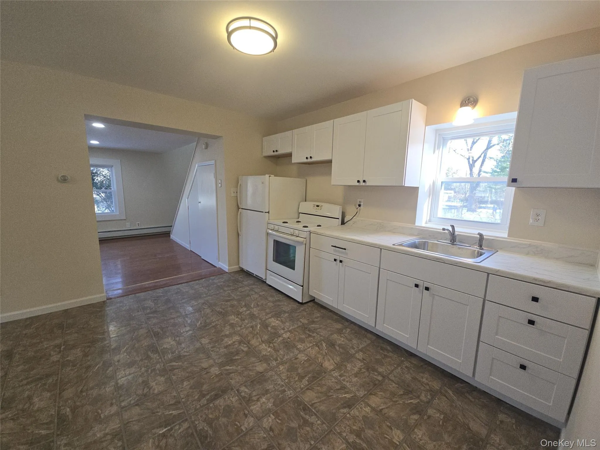Kitchen with white cabinetry, white range, light countertops, and baseboard heating Kitchen with white cabinetry, white range, light countertops, and baseboard heating