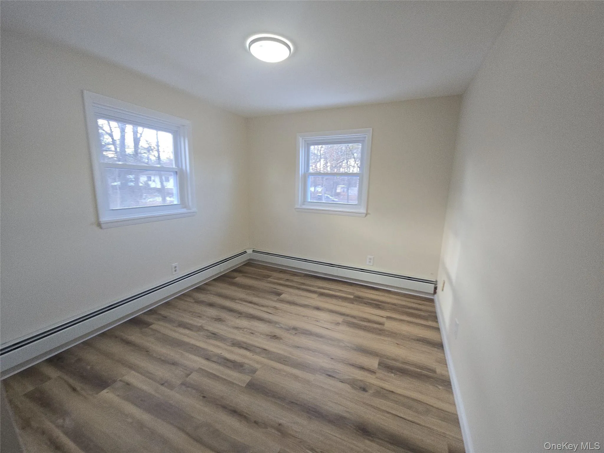 Unfurnished room featuring baseboard heating, wood finished floors, and a baseboard heating unit Unfurnished room featuring baseboard heating, wood finished floors, and a baseboard heating unit