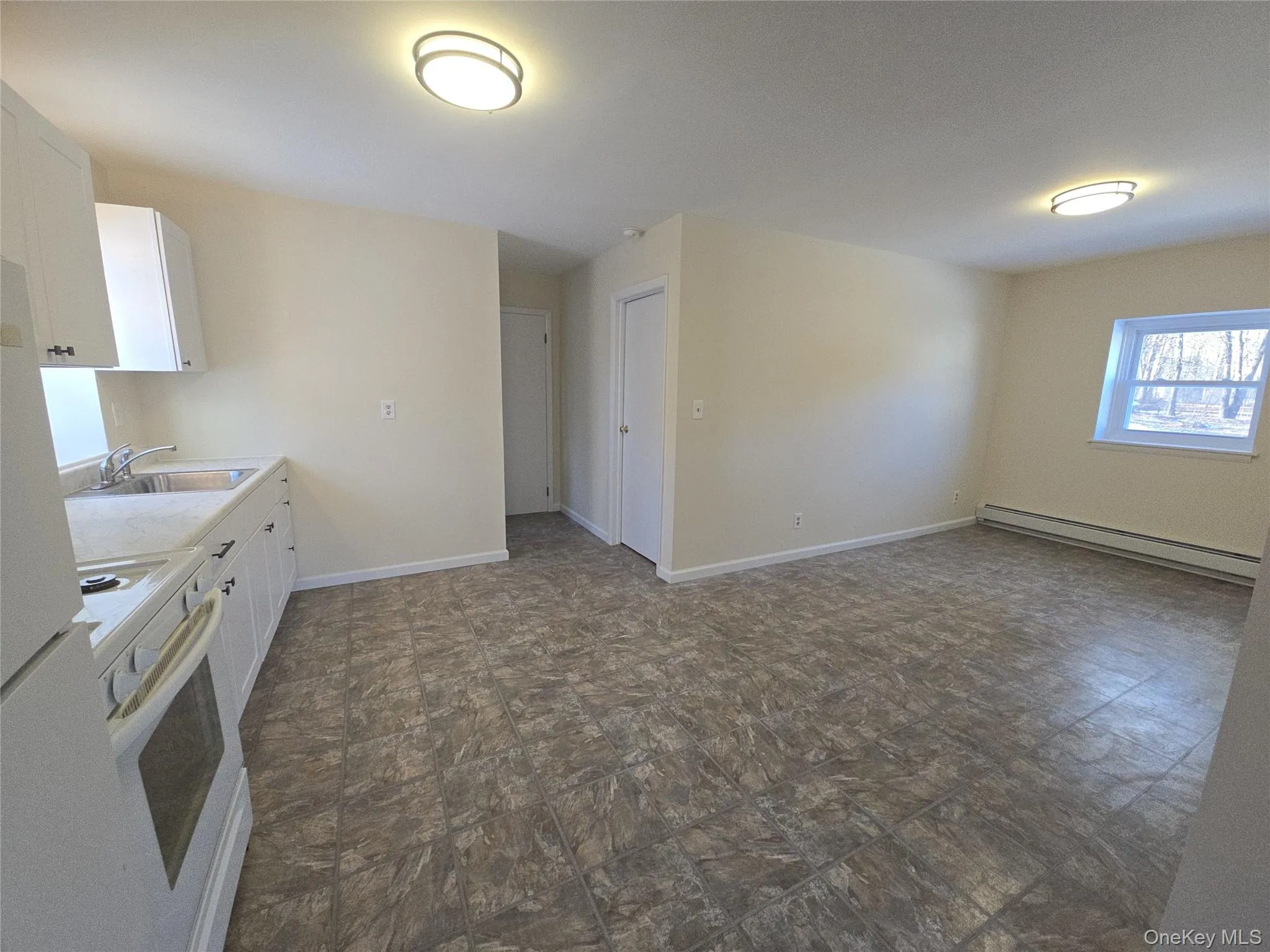 Kitchen with white cabinetry, white appliances, a baseboard radiator, and light countertops Kitchen with white cabinetry, white appliances, a baseboard radiator, and light countertops