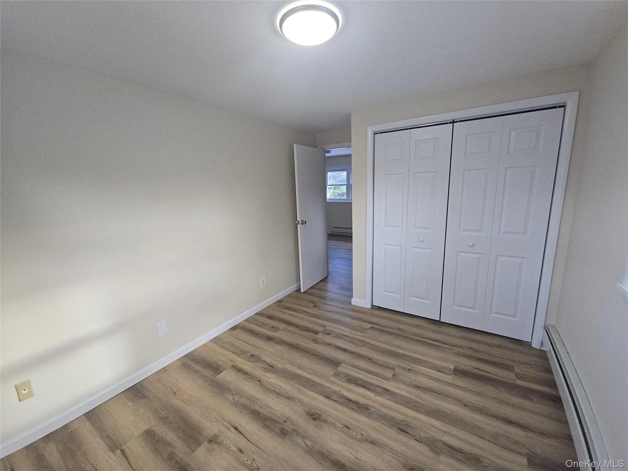 Unfurnished bedroom with a baseboard heating unit, dark wood-style floors, and a closet Unfurnished bedroom with a baseboard heating unit, dark wood-style floors, and a closet