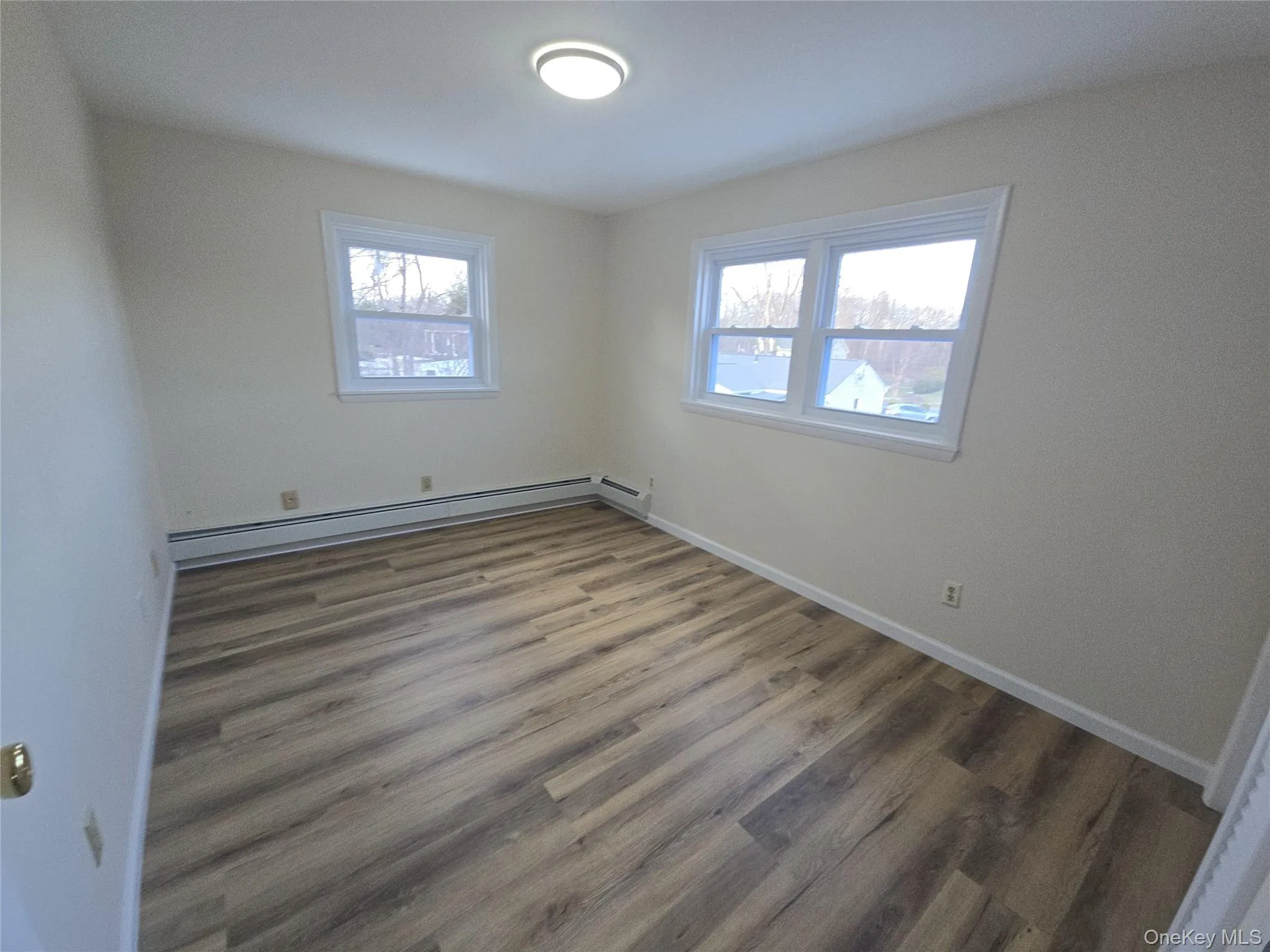 Empty room with a baseboard heating unit, wood finished floors, and plenty of natural light Empty room with a baseboard heating unit, wood finished floors, and plenty of natural light