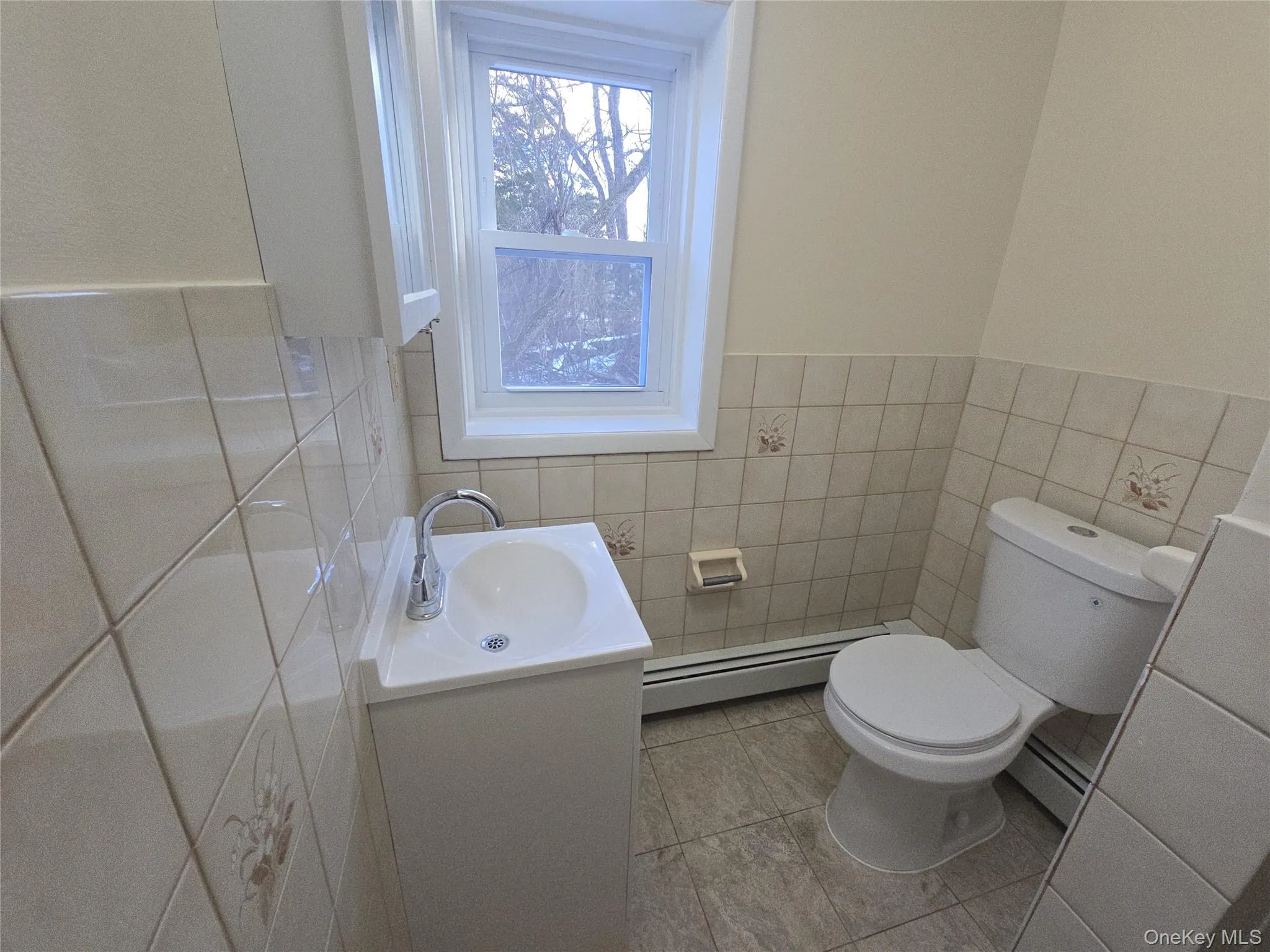 Half bathroom with vanity, a wainscoted wall, a baseboard radiator, and tile walls Half bathroom with vanity, a wainscoted wall, a baseboard radiator, and tile walls