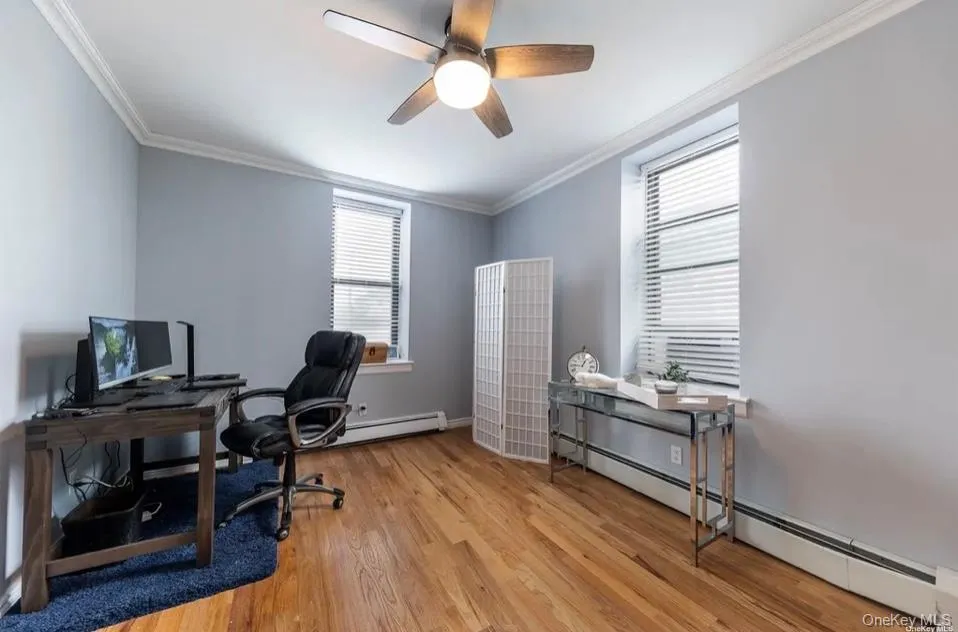 Office area with a baseboard radiator, wood finished floors, ceiling fan, ornamental molding, and baseboard heating Office area with a baseboard radiator, wood finished floors, ceiling fan, ornamental molding, and baseboard heating