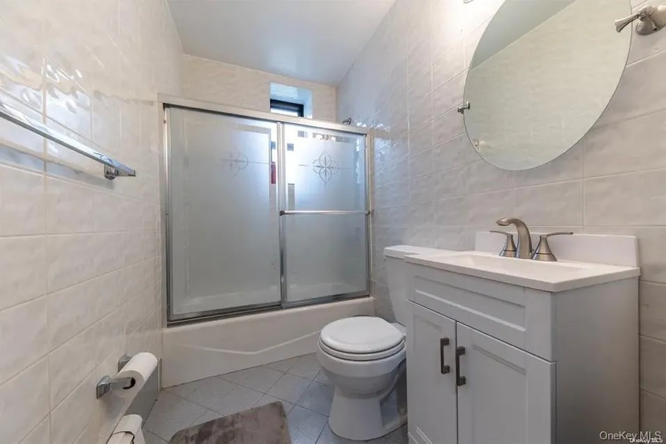 Full bathroom featuring tile walls, tile patterned floors, vanity, and enclosed tub / shower combo Full bathroom featuring tile walls, tile patterned floors, vanity, and enclosed tub / shower combo