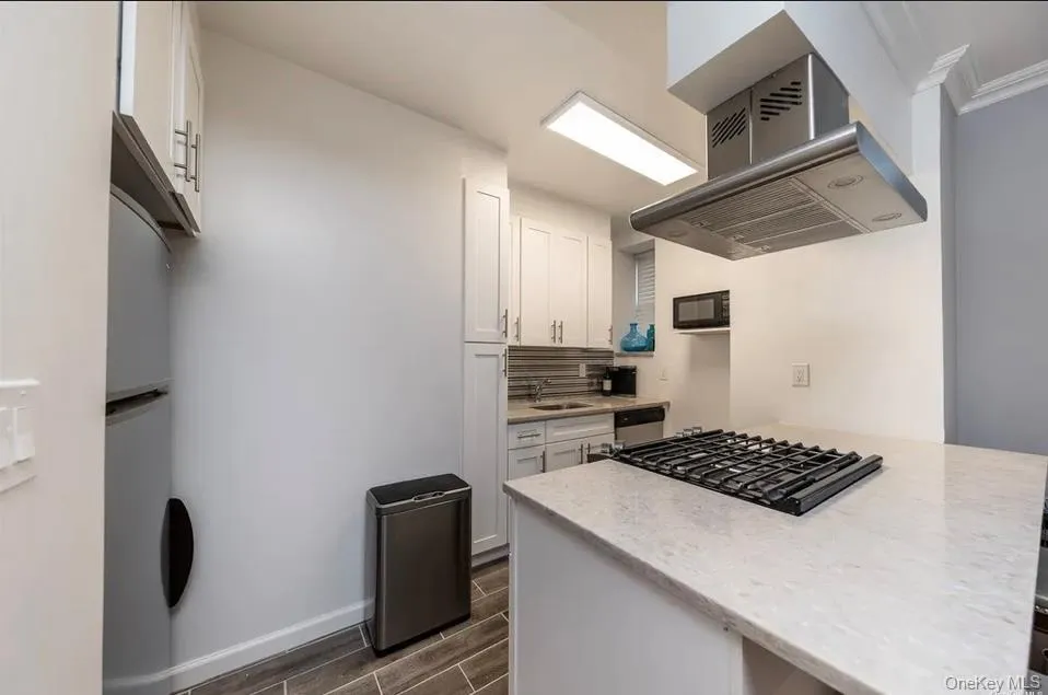 Kitchen with exhaust hood, cooktop, black microwave, wood finish floors, and white cabinetry Kitchen with exhaust hood, cooktop, black microwave, wood finish floors, and white cabinetry