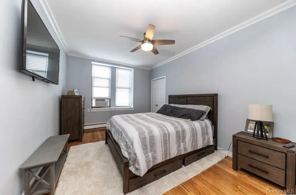 Bedroom featuring baseboard heating, wood finished floors, crown molding, cooling unit, and ceiling fan Bedroom featuring baseboard heating, wood finished floors, crown molding, cooling unit, and ceiling fan