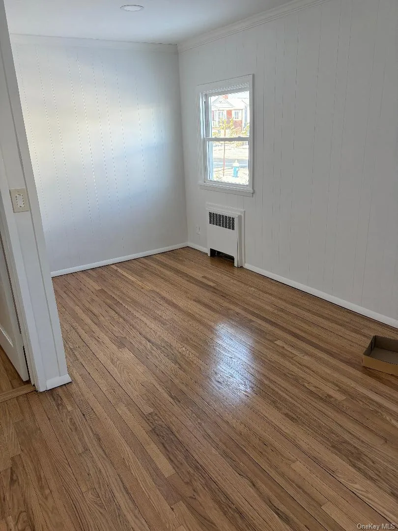 Spare room with wood finished floors, ornamental molding, and radiator Spare room with wood finished floors, ornamental molding, and radiator