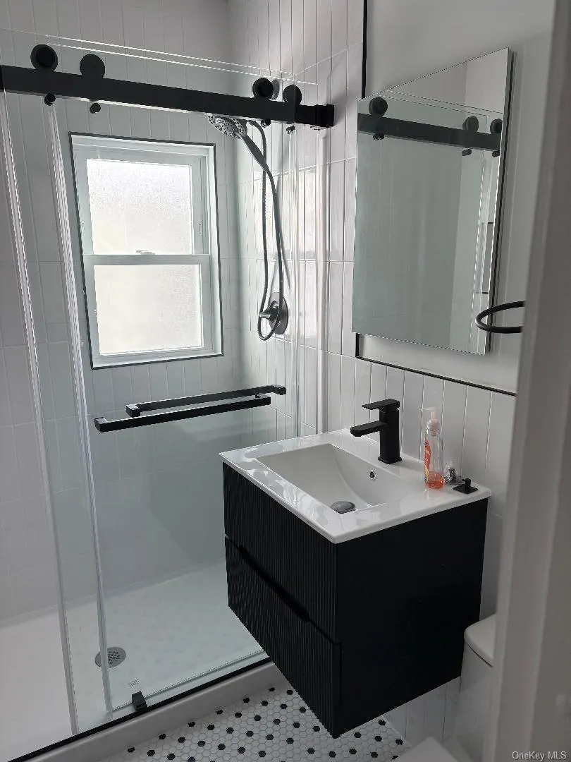 Bathroom with vanity, tile walls, and a shower stall Bathroom with vanity, tile walls, and a shower stall