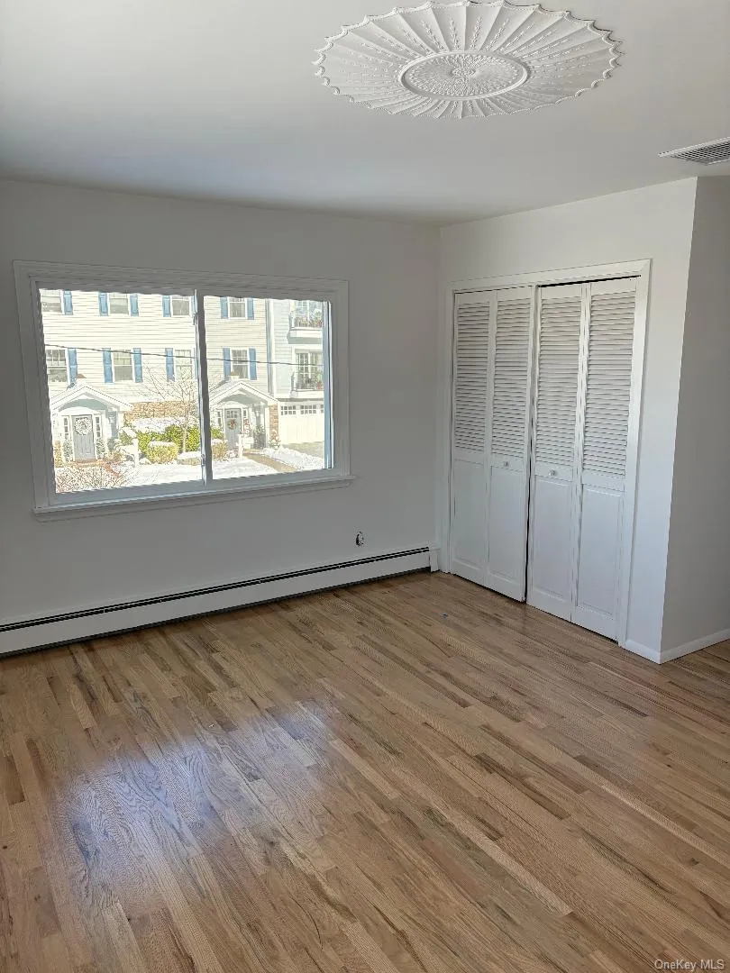Unfurnished bedroom featuring a baseboard radiator, a closet, and light wood-type flooring Unfurnished bedroom featuring a baseboard radiator, a closet, and light wood-type flooring