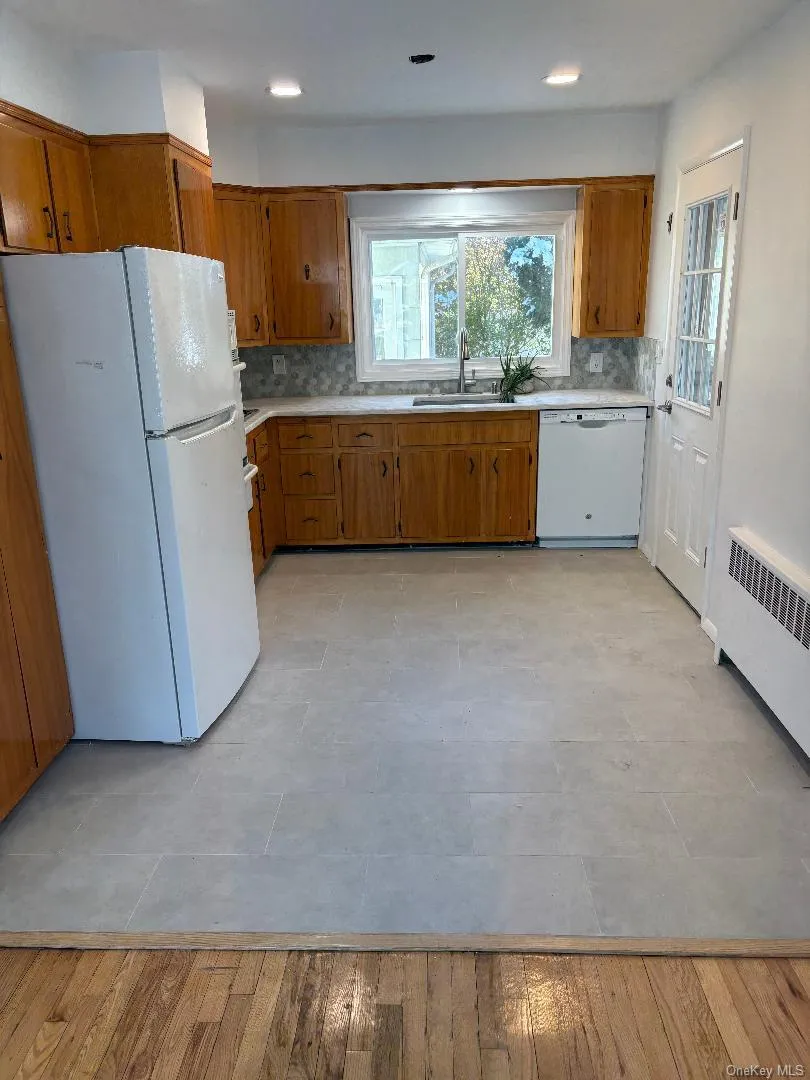 Kitchen with brown cabinetry, white appliances, radiator heating unit, and light countertops Kitchen with brown cabinetry, white appliances, radiator heating unit, and light countertops