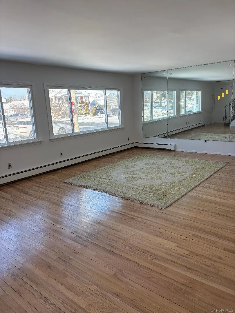 Unfurnished living room with wood-type flooring and a baseboard heating unit Unfurnished living room with wood-type flooring and a baseboard heating unit