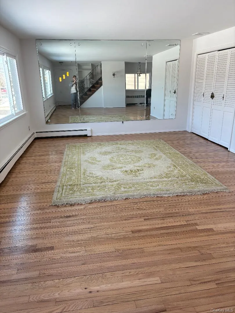 Unfurnished living room with stairway, wood finished floors, a baseboard radiator, and radiator heating unit Unfurnished living room with stairway, wood finished floors, a baseboard radiator, and radiator heating unit