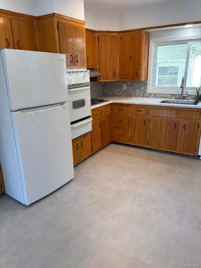Kitchen with white appliances, brown cabinetry, light countertops, and decorative backsplash Kitchen with white appliances, brown cabinetry, light countertops, and decorative backsplash