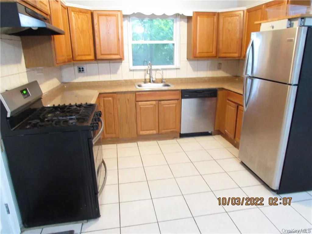 Kitchen featuring stainless steel appliances, under cabinet range hood, light countertops, light tile patterned flooring, and decorative backsplash Kitchen featuring stainless steel appliances, under cabinet range hood, light countertops, light tile patterned flooring, and decorative backsplash