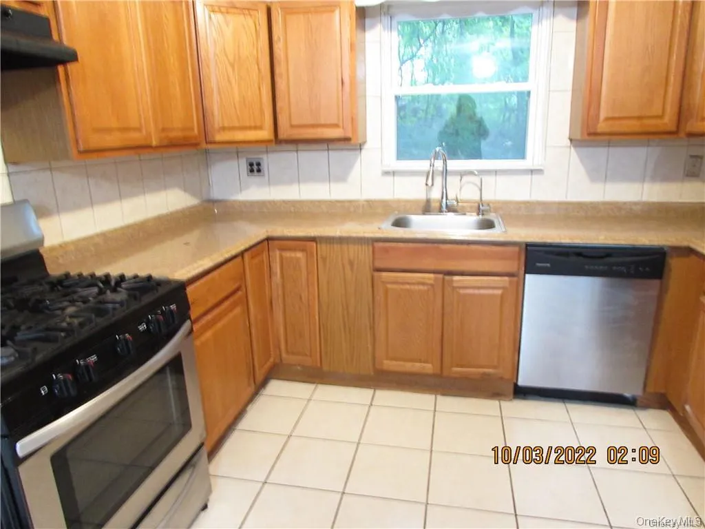 Kitchen with appliances with stainless steel finishes, under cabinet range hood, light countertops, brown cabinets, and light tile patterned flooring Kitchen with appliances with stainless steel finishes, under cabinet range hood, light countertops, brown cabinets, and light tile patterned flooring