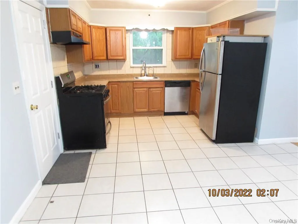 Kitchen featuring stainless steel appliances, range hood, brown cabinets, light countertops, and light tile patterned floors Kitchen featuring stainless steel appliances, range hood, brown cabinets, light countertops, and light tile patterned floors