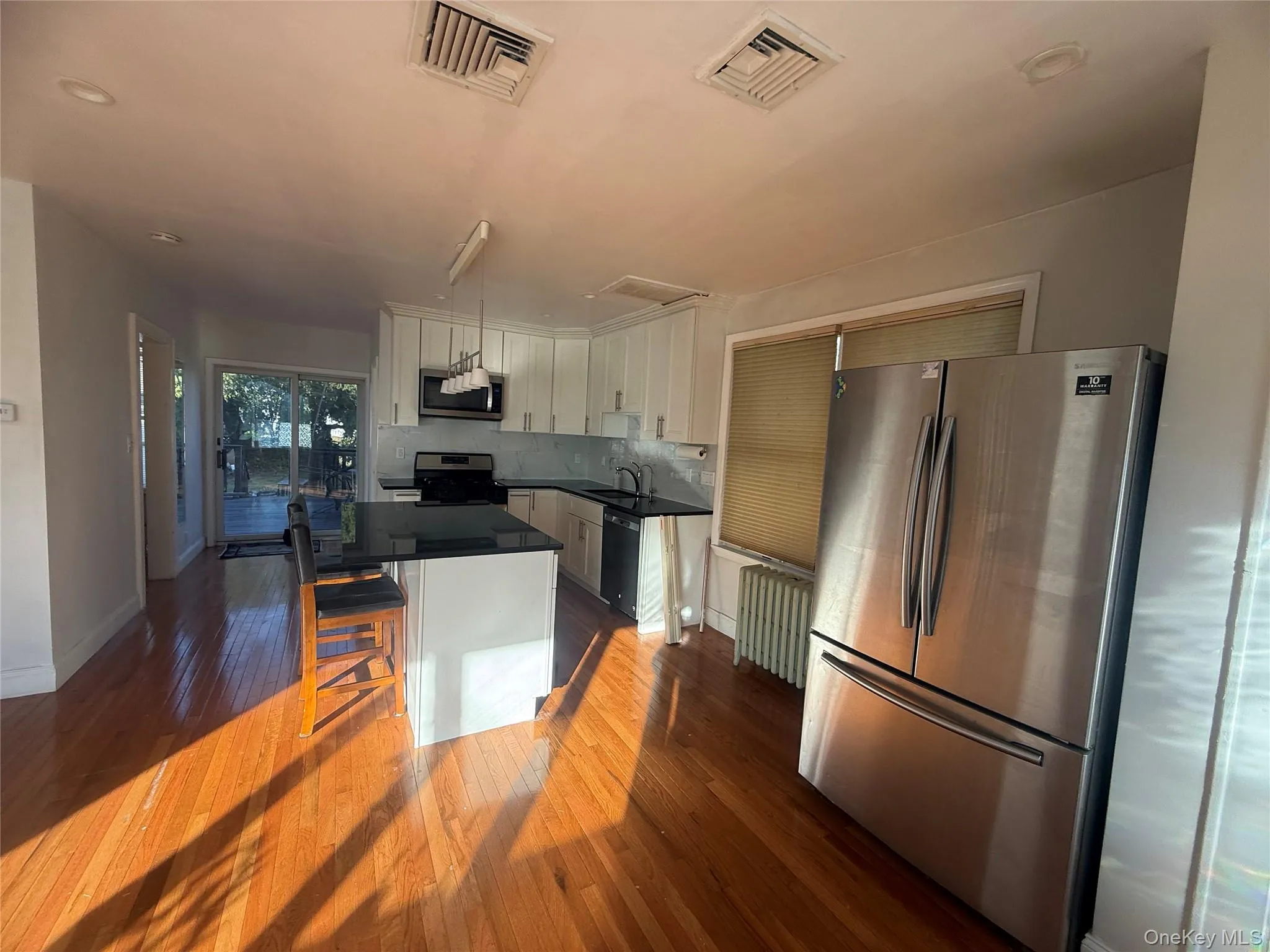 Kitchen with appliances with stainless steel finishes, white cabinets, a center island, a kitchen breakfast bar, and radiator Kitchen with appliances with stainless steel finishes, white cabinets, a center island, a kitchen breakfast bar, and radiator