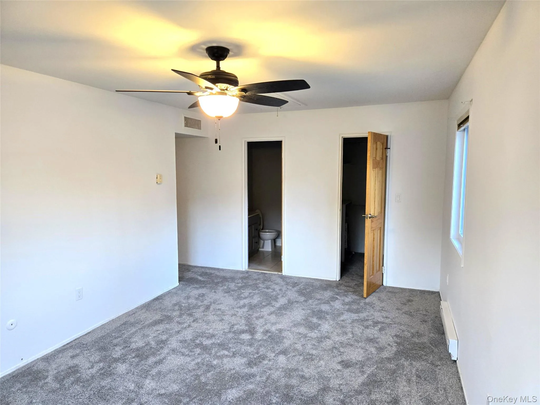 Unfurnished bedroom featuring a walk in closet, carpet floors, ceiling fan, and baseboard heating Unfurnished bedroom featuring a walk in closet, carpet floors, ceiling fan, and baseboard heating