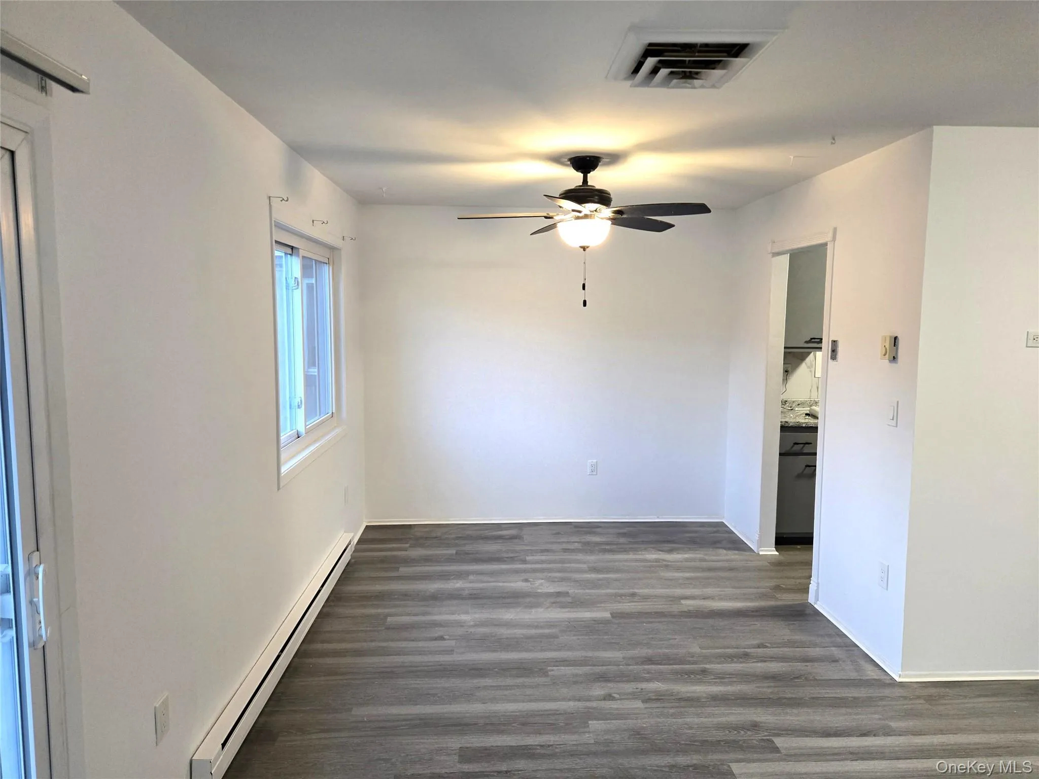 Empty room with baseboard heating, dark wood-type flooring, and ceiling fan Empty room with baseboard heating, dark wood-type flooring, and ceiling fan