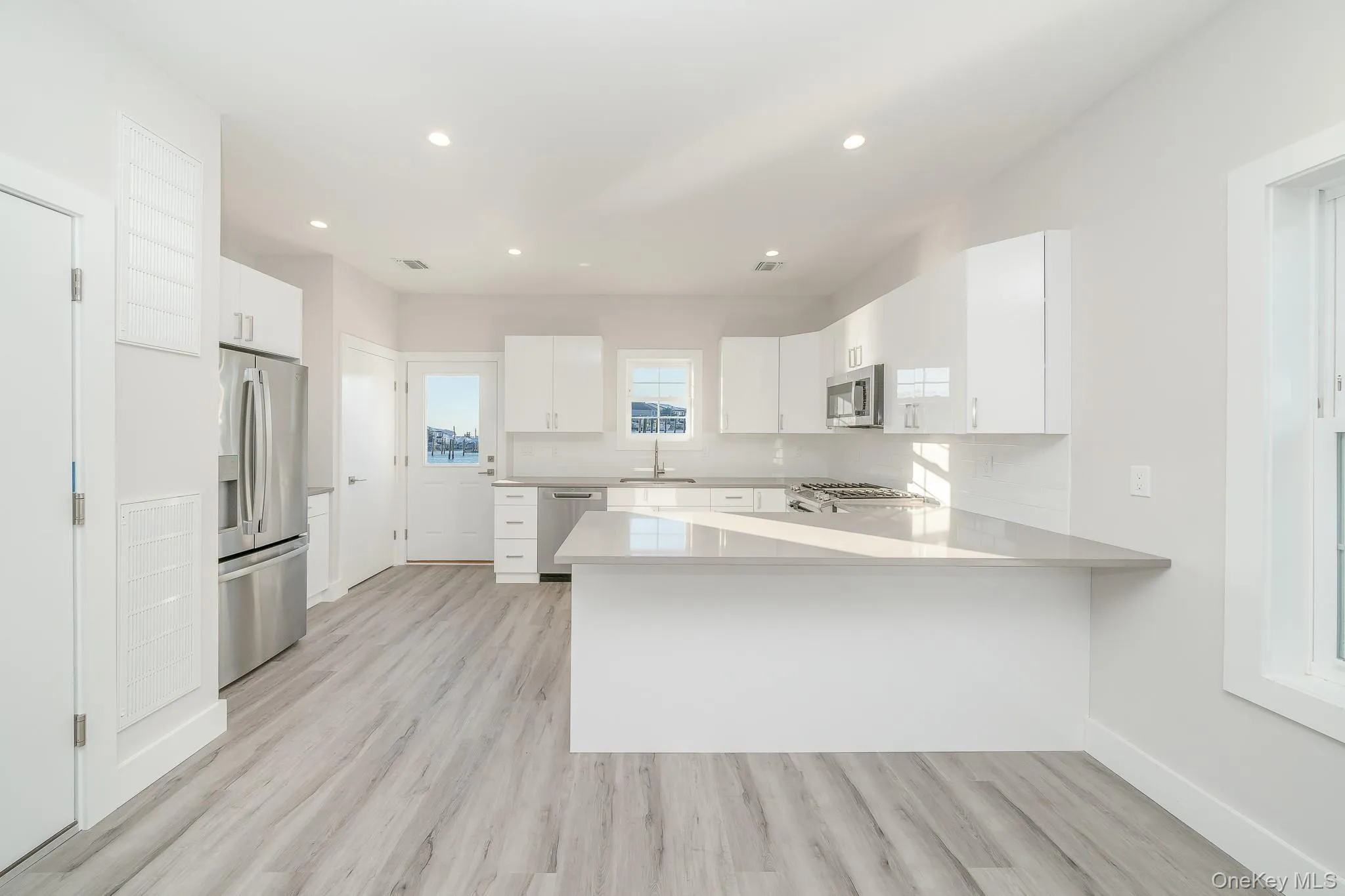 Kitchen featuring white cabinets, a peninsula, stainless steel appliances, light wood finished floors, and recessed lighting Kitchen featuring white cabinets, a peninsula, stainless steel appliances, light wood finished floors, and recessed lighting