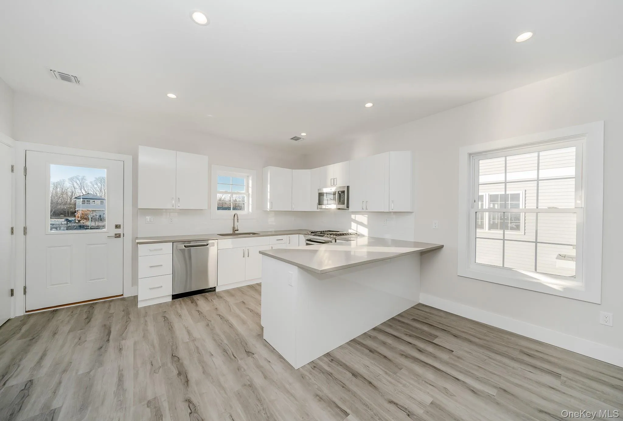 Kitchen with a peninsula, white cabinets, stainless steel appliances, light wood finished floors, and recessed lighting Kitchen with a peninsula, white cabinets, stainless steel appliances, light wood finished floors, and recessed lighting
