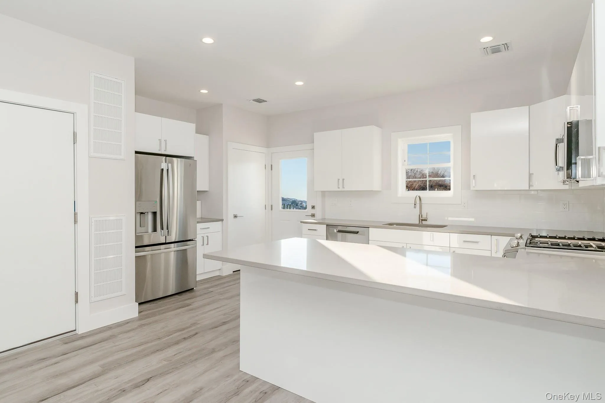Kitchen featuring a peninsula, stainless steel appliances, white cabinetry, light wood-type flooring, and light stone counters Kitchen featuring a peninsula, stainless steel appliances, white cabinetry, light wood-type flooring, and light stone counters