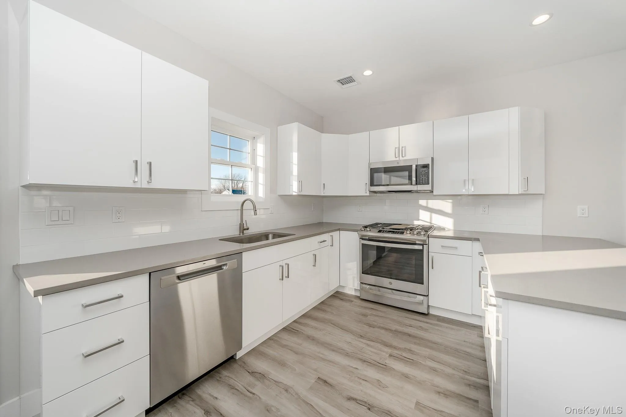 Kitchen featuring appliances with stainless steel finishes, white cabinets, light wood-style flooring, decorative backsplash, and recessed lighting Kitchen featuring appliances with stainless steel finishes, white cabinets, light wood-style flooring, decorative backsplash, and recessed lighting