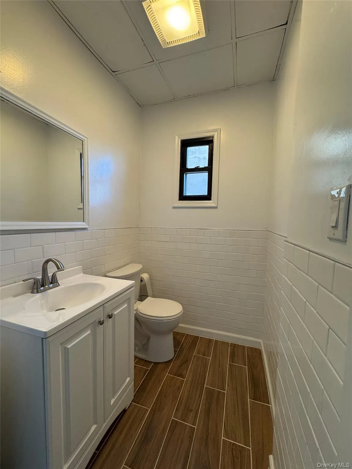 Half bathroom featuring vanity, wood finish floors, a wainscoted wall, and tile walls Half bathroom featuring vanity, wood finish floors, a wainscoted wall, and tile walls