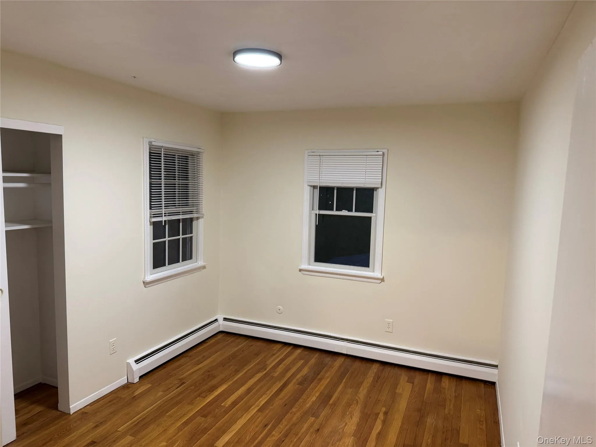 Unfurnished bedroom featuring wood finished floors and a baseboard heating unit Unfurnished bedroom featuring wood finished floors and a baseboard heating unit