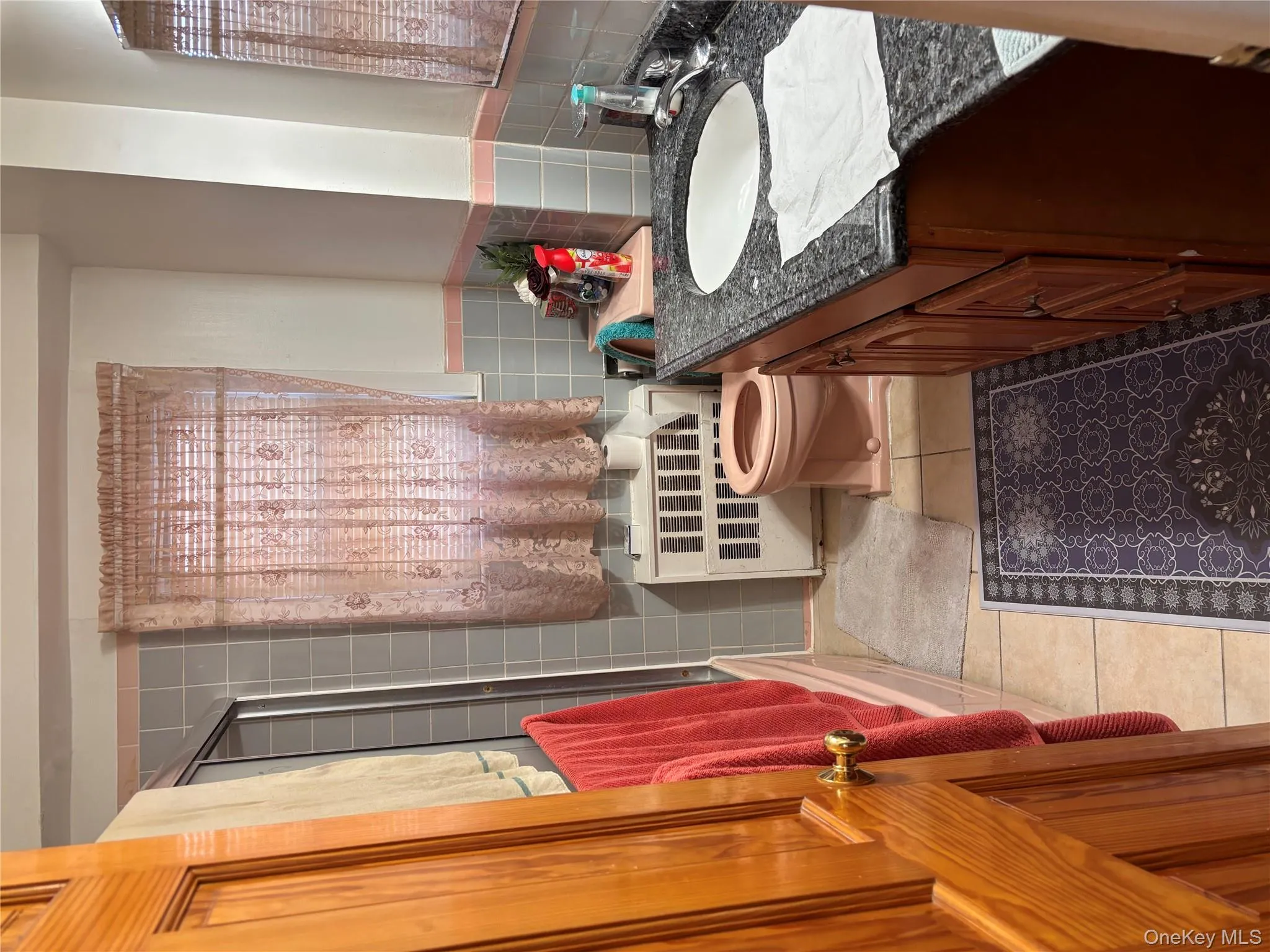 Full bathroom featuring vanity, light tile patterned floors, combined bath / shower with glass door, tile walls, and a wainscoted wall Full bathroom featuring vanity, light tile patterned floors, combined bath / shower with glass door, tile walls, and a wainscoted wall
