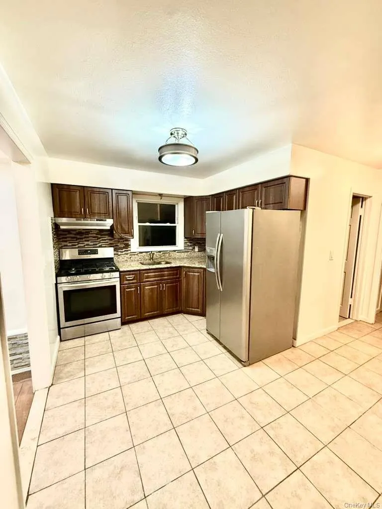 Kitchen with stainless steel appliances, dark brown cabinets, light tile patterned floors, and under cabinet range hood Kitchen with stainless steel appliances, dark brown cabinets, light tile patterned floors, and under cabinet range hood