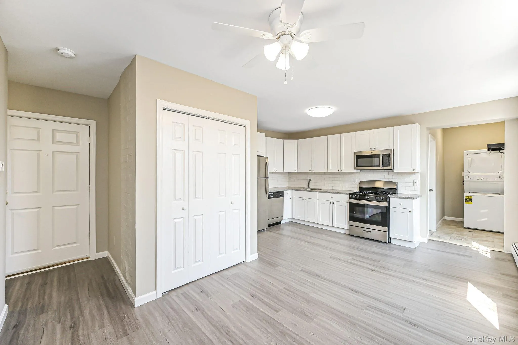 Kitchen featuring stacked washer and clothes dryer, stainless steel appliances, white cabinets and ceiling fan Kitchen featuring stacked washer and clothes dryer, stainless steel appliances, white cabinets and ceiling fan