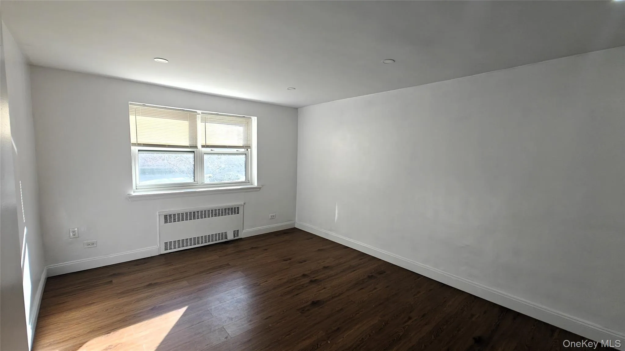 Unfurnished room featuring radiator heating unit, dark wood-type flooring, and recessed lighting Unfurnished room featuring radiator heating unit, dark wood-type flooring, and recessed lighting