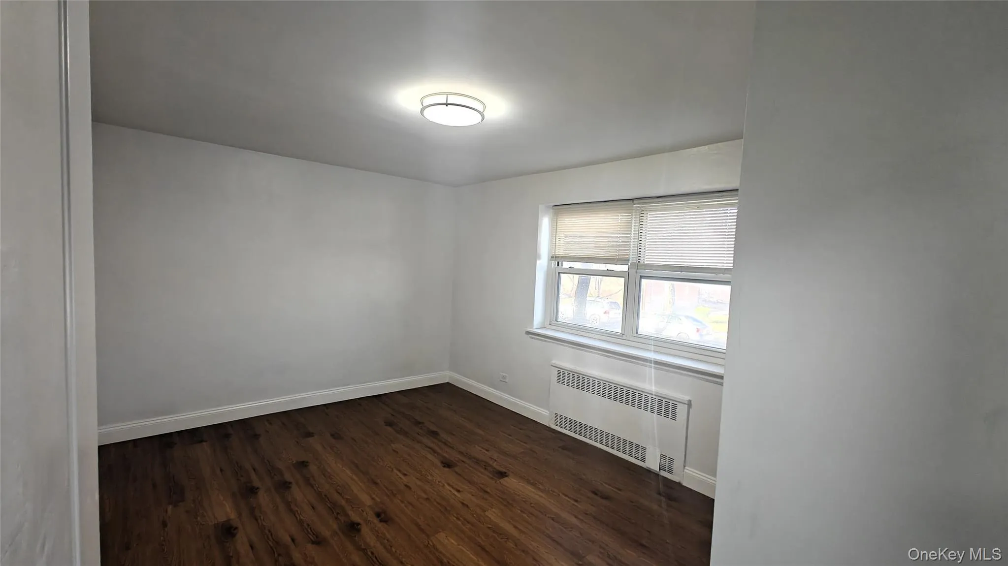 Empty room with radiator and dark wood-style floors Empty room with radiator and dark wood-style floors
