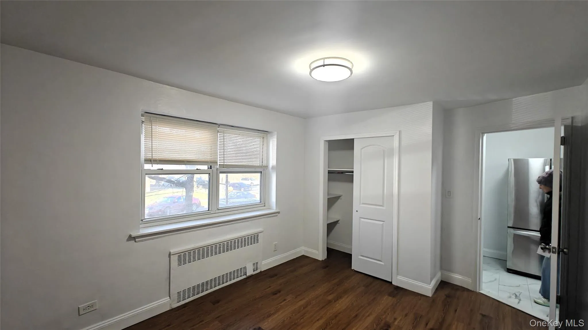 Unfurnished bedroom with radiator heating unit, freestanding refrigerator, dark wood-style flooring, and a closet Unfurnished bedroom with radiator heating unit, freestanding refrigerator, dark wood-style flooring, and a closet