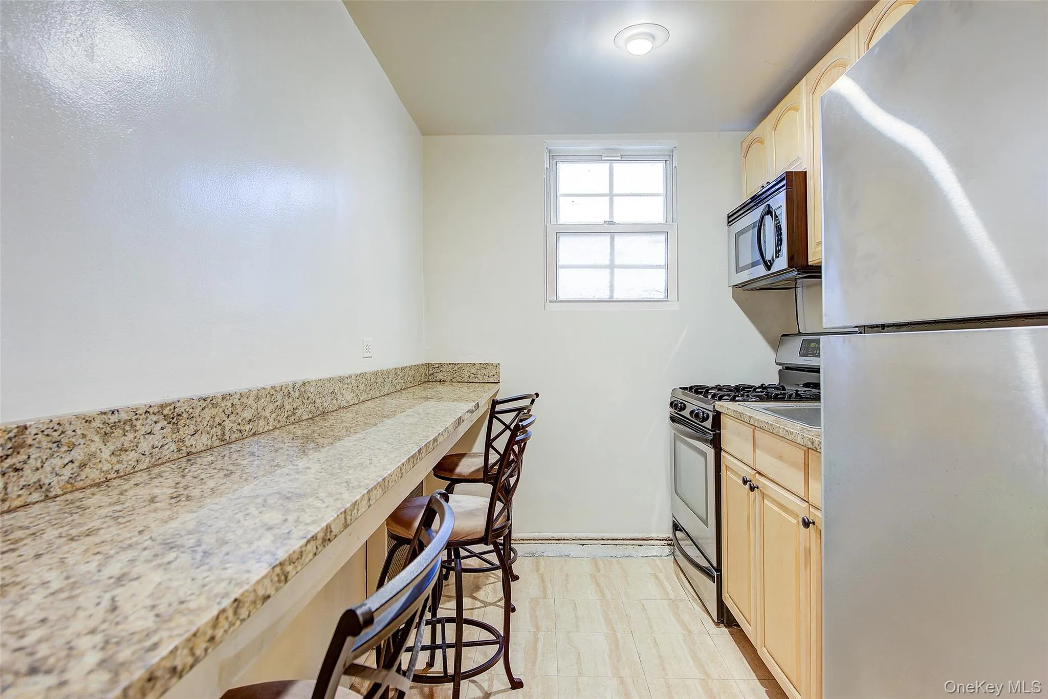 Kitchen featuring appliances with stainless steel finishes, light brown cabinets, a breakfast bar, and light flooring Kitchen featuring appliances with stainless steel finishes, light brown cabinets, a breakfast bar, and light flooring