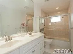 Full bathroom with double vanity, shower / bath combination with glass door, and light tile patterned floors Full bathroom with double vanity, shower / bath combination with glass door, and light tile patterned floors
