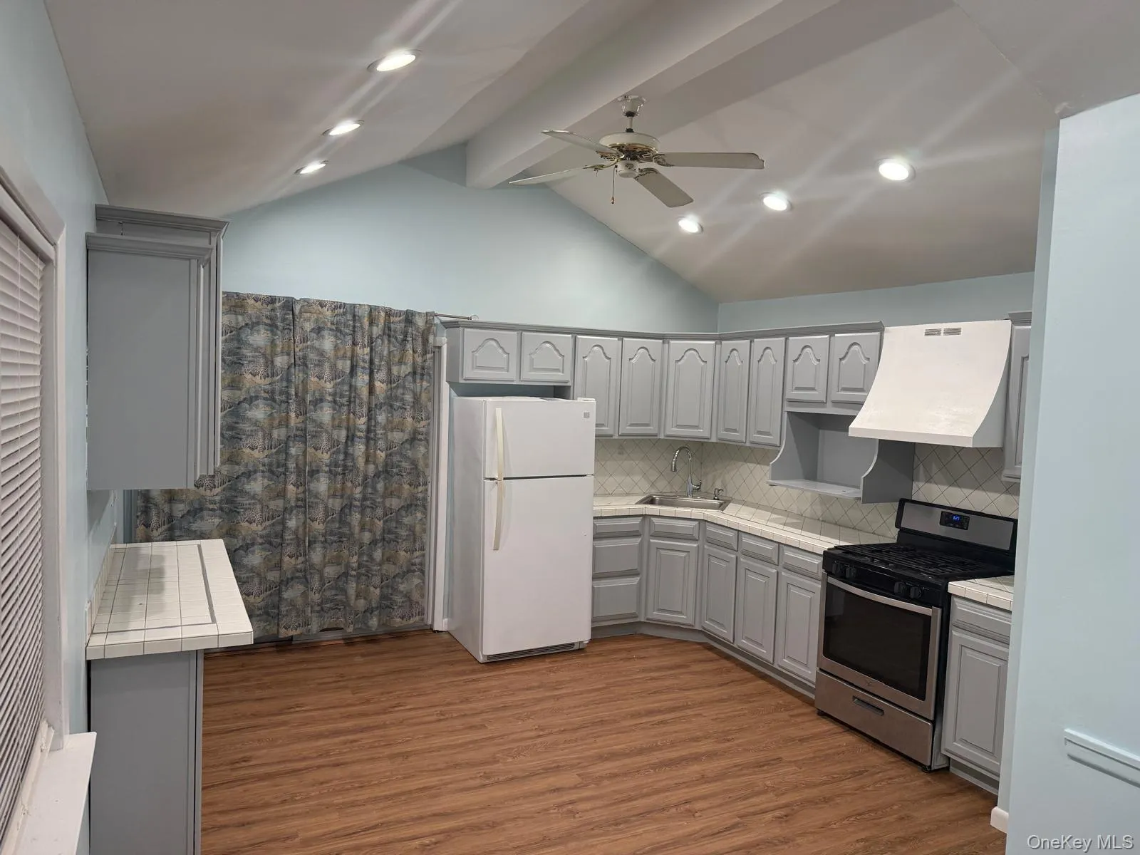 Kitchen featuring gray cabinets, stainless steel range with gas stovetop, freestanding refrigerator, custom exhaust hood, and dark wood-style flooring Kitchen featuring gray cabinets, stainless steel range with gas stovetop, freestanding refrigerator, custom exhaust hood, and dark wood-style flooring