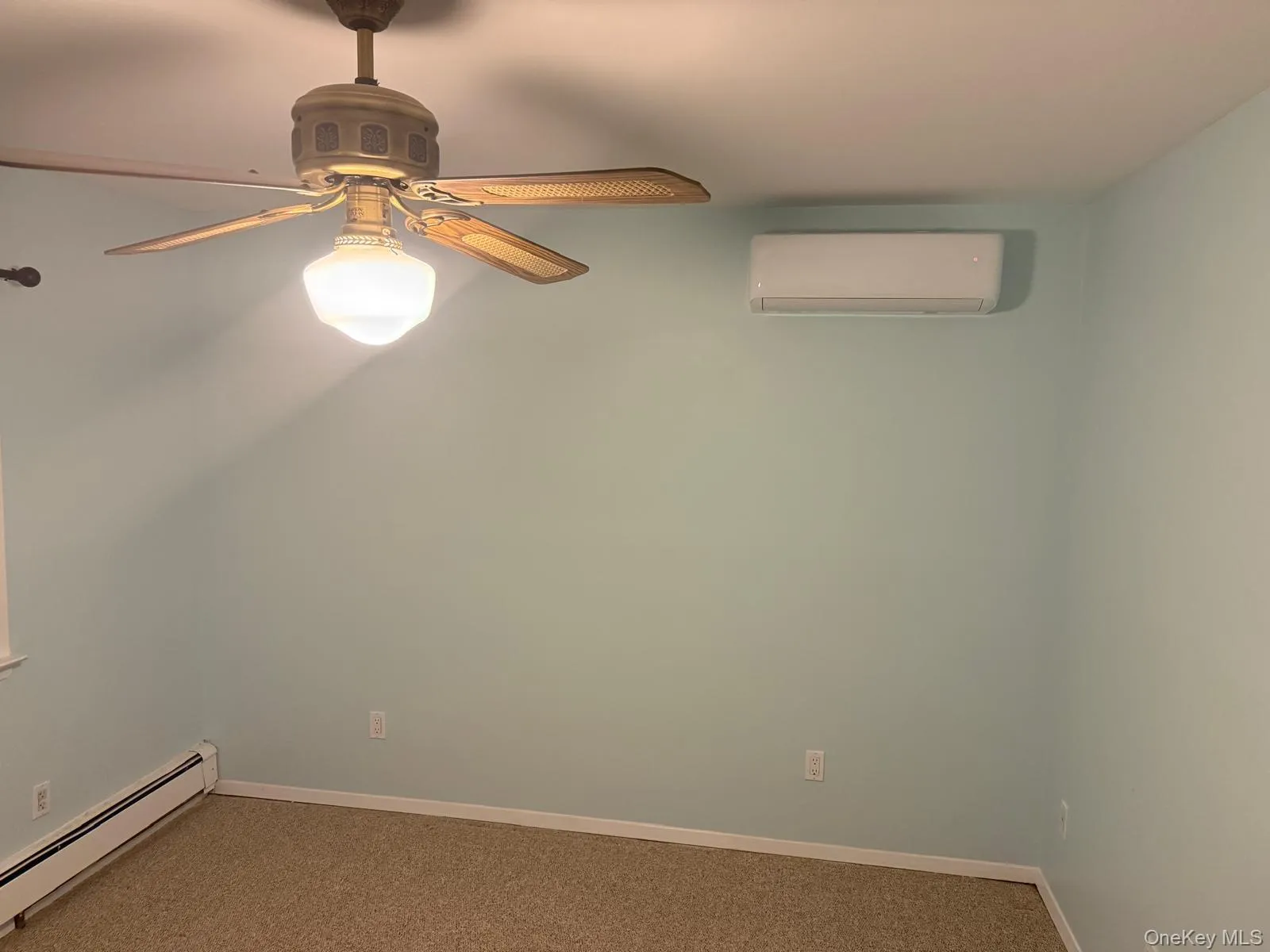 Carpeted empty room with a baseboard radiator, an AC wall unit, and a ceiling fan Carpeted empty room with a baseboard radiator, an AC wall unit, and a ceiling fan